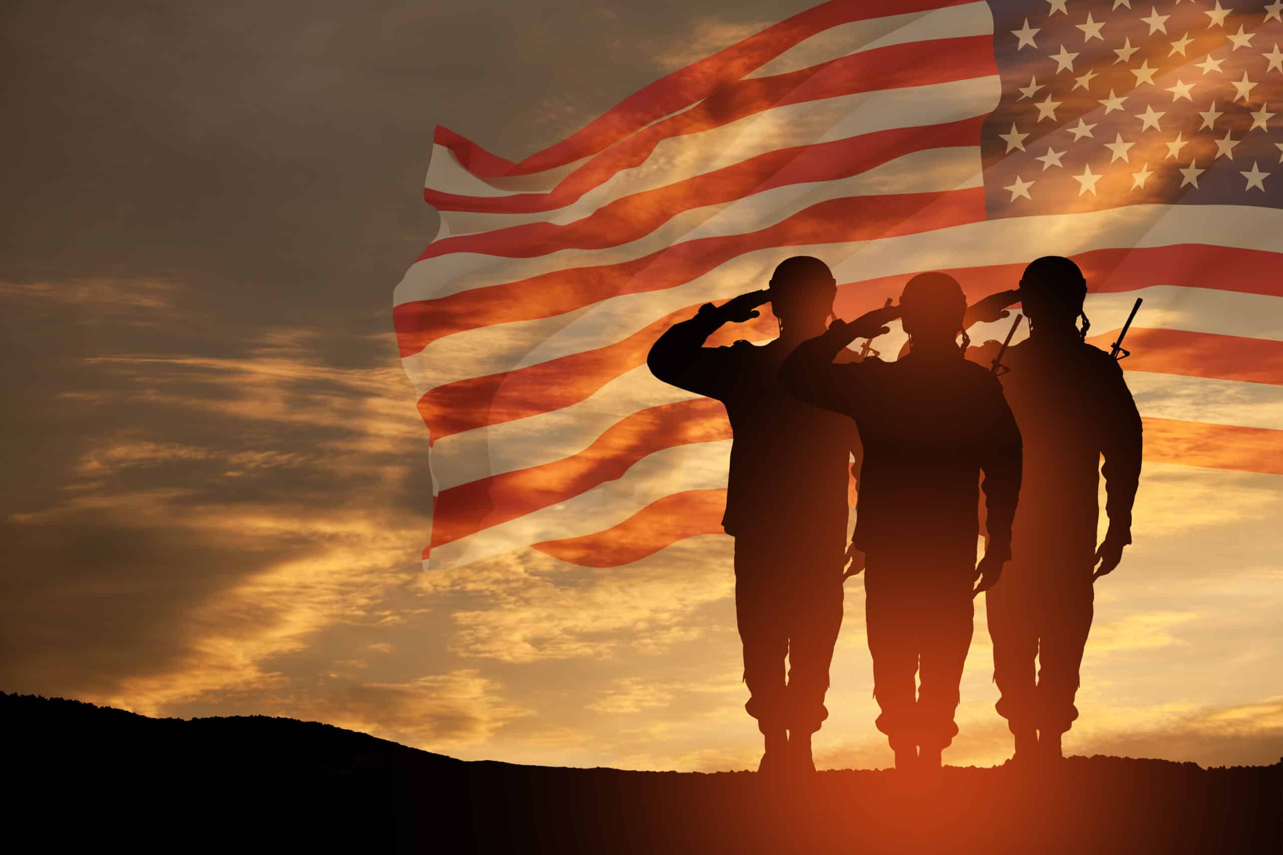 Three soldiers salute at sunset, silhouetted against a large, waving American flag in the sky. The dramatic, orange-tinted background sets the scene for a powerful veterans benefits presentation.