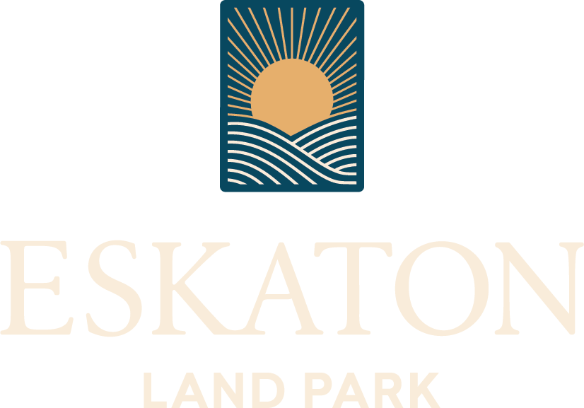 A stylized logo featuring a golden sun rising over wavy lines, set within a dark rectangle. Below, the faded text reads “ESKATON LAND PARK.”.