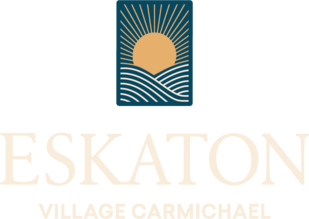 A logo featuring a stylized sun rising over hills, with ESKATON VILLAGE CARMICHAEL written underneath in light, elegant font.