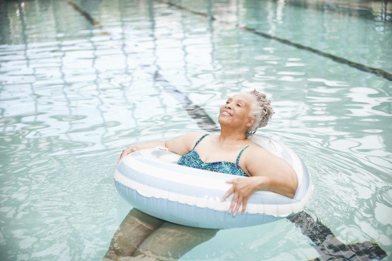An Eskaton Village Placerville resident enjoys a relaxing experience, smiling as she floats in a clear swimming pool with a white and blue inflatable ring, surrounded by inviting swimming lanes.