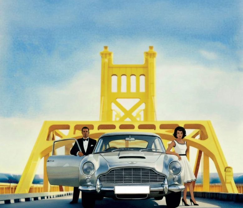 A man in a tuxedo and a woman in a white dress stand by a classic silver car on a bright yellow bridge under a blue sky. The man stands with the car door open, while the woman is beside the hood.