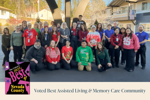 A large group of smiling people, some in festive attire, pose outdoors for a group photo. An emblem reads Best of Nevada County 2023. Text below says, Voted Best Assisted Living & Memory Care Community.
