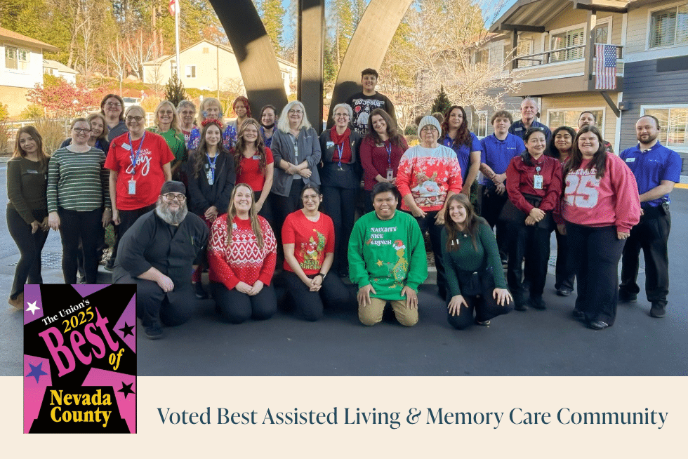 A large group of smiling people, some in festive attire, pose outdoors for a group photo. An emblem reads Best of Nevada County 2023. Text below says, Voted Best Assisted Living & Memory Care Community.