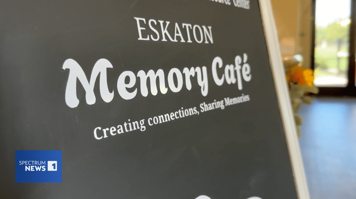 A chalkboard sign reads ESKATON Memory Café: Creating connections, Sharing Memories. The Spectrum News 1 logo appears in the bottom left corner.