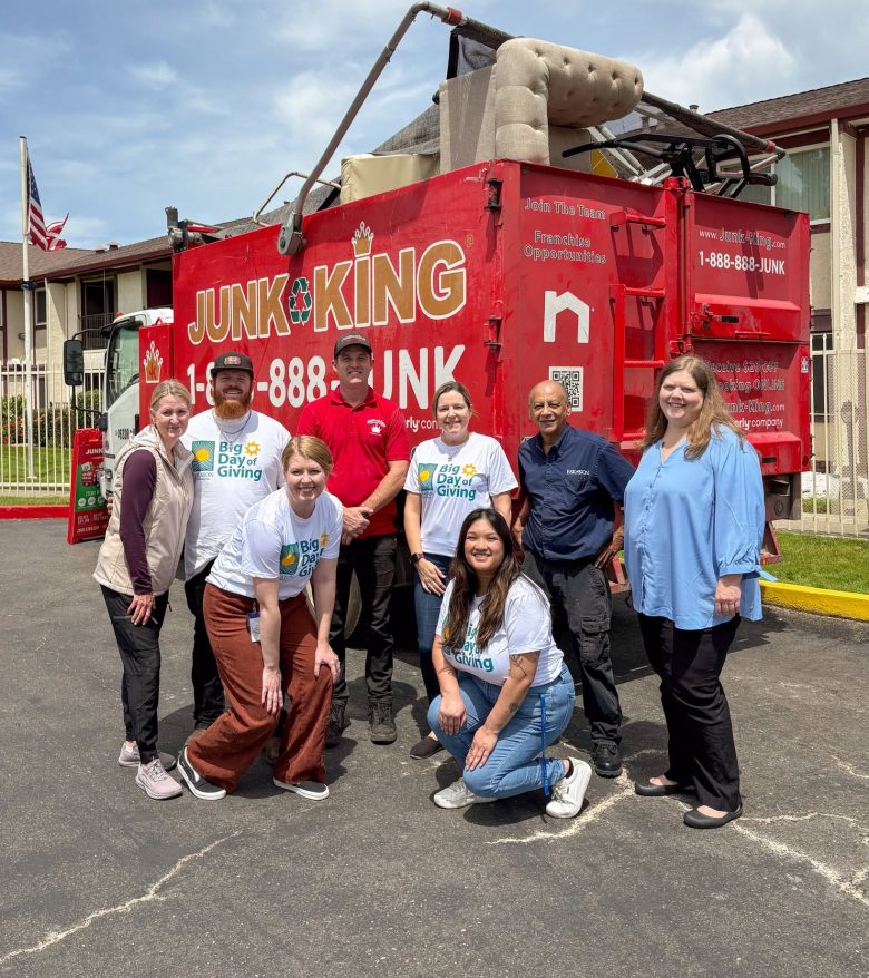 Nine people stand and kneel in front of a red Junk King truck outside a building. Some wear Big Day of Giving shirts, highlighting their involvement with Eskaton volunteer opportunities. The group smiles at the camera on a sunny day.