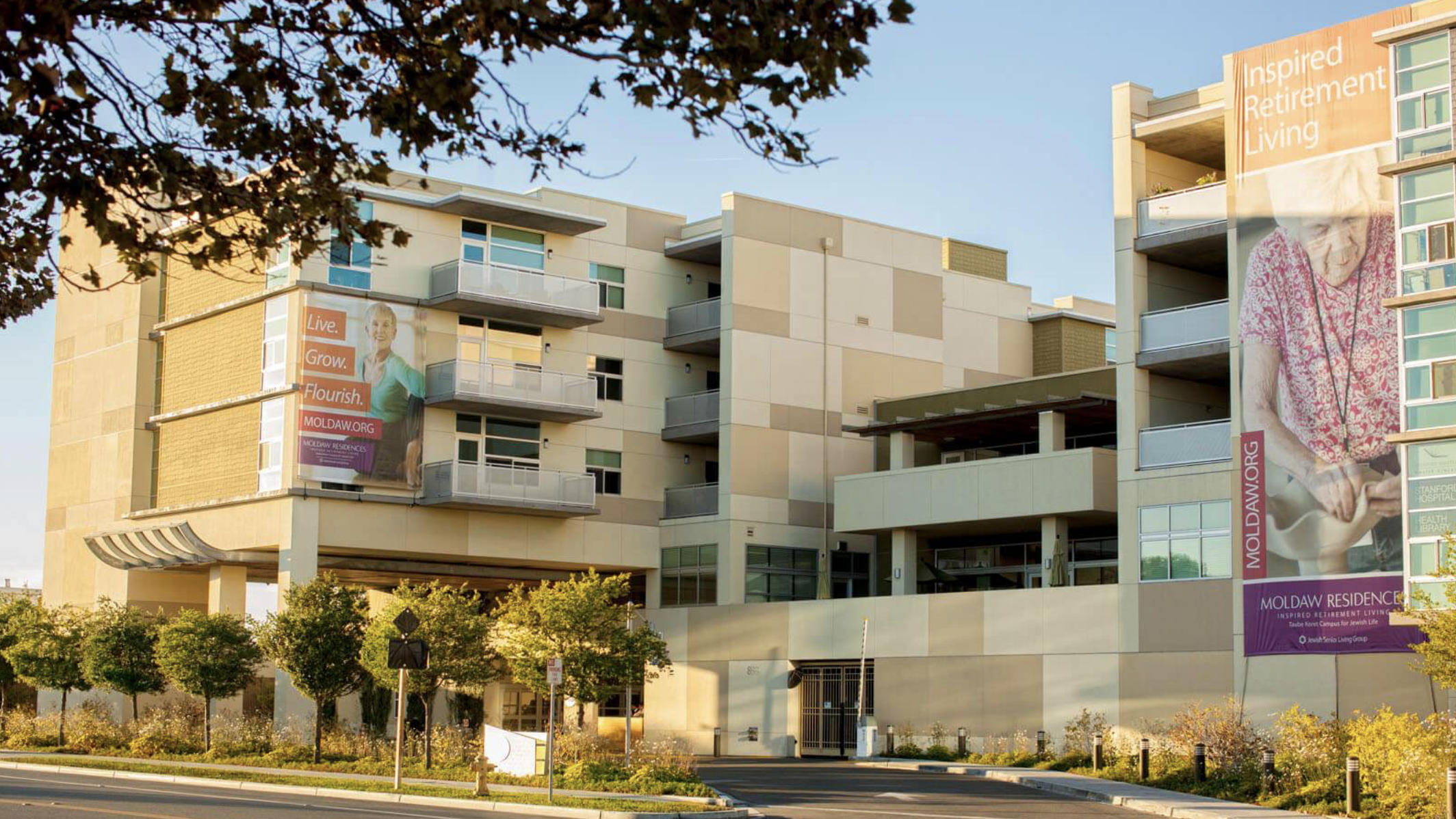 Exterior of the multi-story Moldaw Residences retirement community building with large banners reading Inspired Retirement Living and Live. Grow. Flourish.